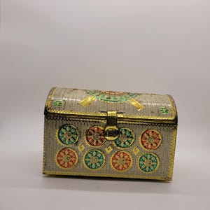Puede incluir: Un cofre decorativo plateado con tapa curvada y ribetes dorados. El cofre presenta dise&ntilde;os florales coloridos en rojo, verde y dorado. Un cierre dorado asegura la parte delantera, ideal para guardar joyas o peque&ntilde;os objetos. Mide unos 15 cm de largo.