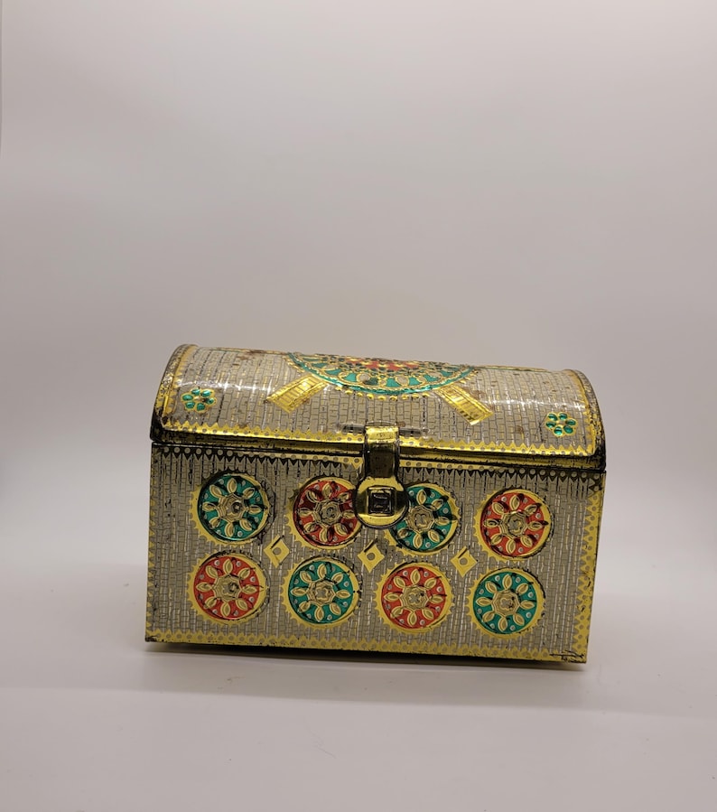 Puede incluir: Un cofre decorativo plateado con tapa curvada y ribetes dorados. El cofre presenta dise&ntilde;os florales coloridos en rojo, verde y dorado. Un cierre dorado asegura la parte delantera, ideal para guardar joyas o peque&ntilde;os objetos. Mide unos 15 cm de largo.