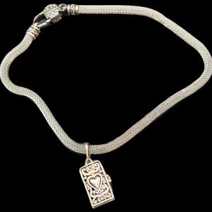 May include: A silver-toned mesh chain necklace featuring a rectangular pendant with an embossed heart design and intricate scrollwork. The necklace includes a decorative clasp with a cross motif, showcasing a metallic finish and a flexible link structure.