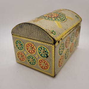 Puede incluir: Un cofre decorativo de metal con tapa abovedada. El cofre es plateado con ribetes dorados y presenta dise&ntilde;os florales coloridos en rojo, verde y amarillo. El cofre tiene una base rectangular y una parte superior curva.