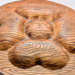May include: A brown, wood-grain-textured serving platter with five sections. The platter is made by Treasure Craft U.S.A. and has a circular shape. The sections are raised and have a natural wood appearance.