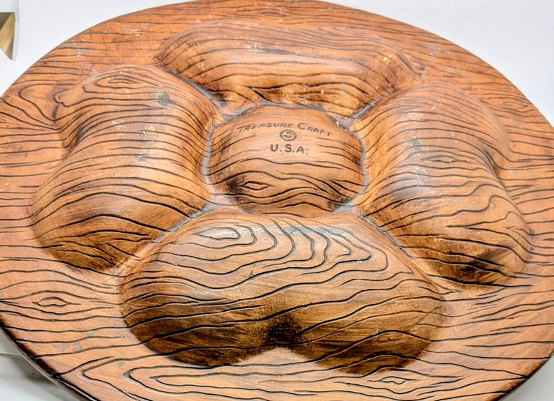 May include: A brown, wood-grain-textured serving platter with five sections. The platter is made by Treasure Craft U.S.A. and has a circular shape. The sections are raised and have a natural wood appearance.