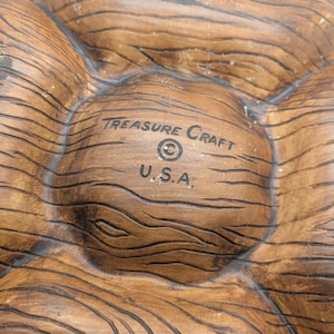 May include: A brown, wooden-textured serving dish with multiple compartments. The dish is marked with the text "TREASURE CRAFT" and "U.S.A.". The dish has a rustic, natural appearance, suitable for serving snacks or appetizers.
