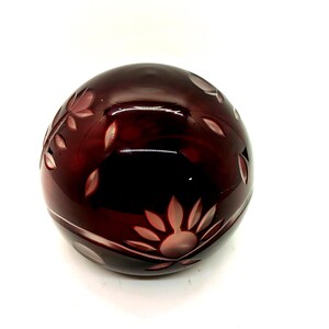May include: A round, dark red glass object with etched floral designs. The glass has a glossy finish and the etched patterns are white. The object is set against a white background.