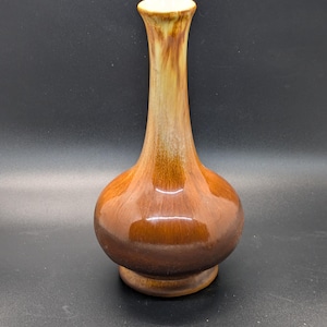 May include: A brown ceramic vase with a bulbous base and a slender neck. The vase has a glossy finish and a gradient of colors, transitioning from a light beige at the top to a dark brown at the base. The vase is approximately 8 inches tall.