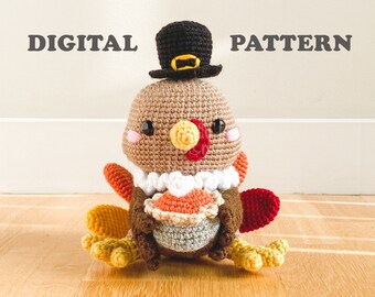 May include: A crochet turkey amigurumi wearing a black pilgrim hat with a yellow buckle, featuring a tan head, white neck ruff, and colorful tail feathers. The turkey holds a small pie. The text DIGITAL PATTERN is visible above the turkey.