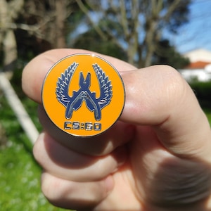 May include: Orange and silver CS:GO pin with a black and silver logo of two crossed knives with wings.