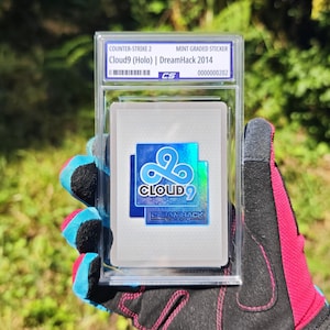 Può includere: Un adesivo Cloud9 Holo DreamHack 2014 di Counter-Strike 2, classificato mint e sigillato in una custodia protettiva in plastica trasparente. L'adesivo presenta un logo blu con il testo Cloud9 e DreamHack 2014, con una finitura olografica.