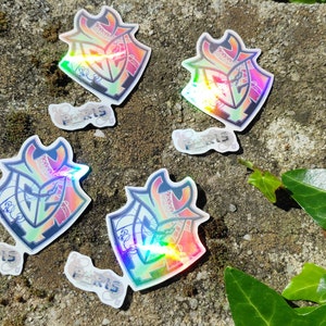 May include: Five iridescent holographic stickers with a black and green logo and the word "Paris" printed on them. The stickers are on a gray, textured surface.