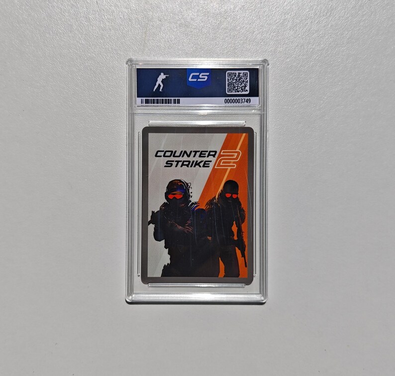 Puede incluir: Una tarjeta coleccionable calificada con el logotipo de Counter-Strike 2 y dos figuras con equipo t&aacute;ctico. La tarjeta est&aacute; dentro de un soporte de pl&aacute;stico transparente con una etiqueta azul y blanca en la parte superior.