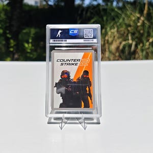 Puede incluir: Una tarjeta coleccionable calificada con el logotipo del juego "Counter-Strike 2" y una ilustraci&oacute;n de dos figuras con equipo t&aacute;ctico. La tarjeta est&aacute; dentro de un soporte de pl&aacute;stico transparente con un logotipo "CS" y un n&uacute;mero de serie.