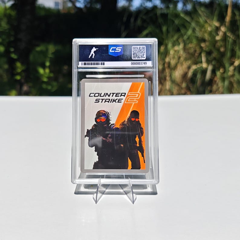 Puede incluir: Una tarjeta coleccionable calificada con el logotipo del juego "Counter-Strike 2" y una ilustraci&oacute;n de dos figuras con equipo t&aacute;ctico. La tarjeta est&aacute; dentro de un soporte de pl&aacute;stico transparente con un logotipo "CS" y un n&uacute;mero de serie.