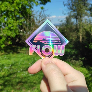 May include: A holographic sticker with a sunset and mountains design. The sticker is in a diamond shape and says "FLOW" in bold letters.