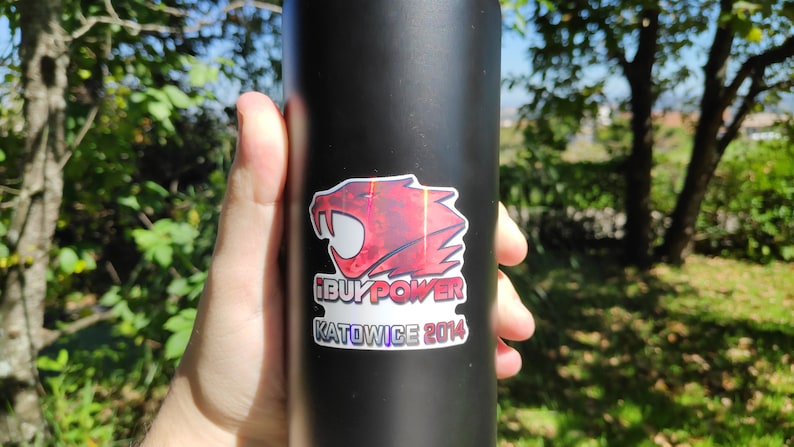 May include: A black water bottle with a red, white, and blue sticker featuring a red and black creature with the text "iBUYPOWER KATOWICE 2014".