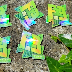 May include: Five holographic stickers with a green and yellow color scheme. The stickers feature the letters "FB" in a stylized font. The stickers have the text "E-League Atlanta 2017" printed on them.