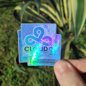 May include: Two iridescent stickers with the Cloud9 logo and the text "Cloud9" and "Teamhack" in a blue, green, and purple color scheme.