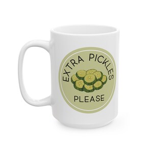 May include: White ceramic mug with a green and white circle design. The circle says "Extra Pickles Please" with a drawing of pickle slices inside.