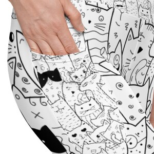 May include: White leggings with a black and white cat pattern. The leggings feature a pocket on the side and a high waistband. The cat design includes various cat illustrations with different expressions and patterns.
