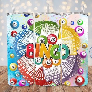 May include: Three tall, insulated tumblers with lids and straws, featuring a colorful bingo-themed design. The design includes bingo balls, cards, and the word "BINGO" in large, bold letters. The tumblers are decorated with various numbers and bingo-related graphics.
