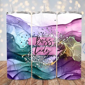 May include: A cylindrical tumbler with a straw featuring an abstract alcohol ink design in shades of purple, teal, and pink. The center displays the text Boss Lady in black script over a pink brushstroke, accented with silver glitter and gold veins.