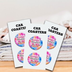 May include: Three car coaster sets. Each set features a round coaster with a colorful tie-dye design and the text "OVER STIMULATED MOMS CLUB". The coasters are displayed on white cards with the words "CAR COASTERS" printed in black.