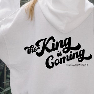 以下が含まれることがあります： 背面に「The King is Coming」という黒い文字と聖書の引用「Revelation 22:12」が書かれた白いパーカー。