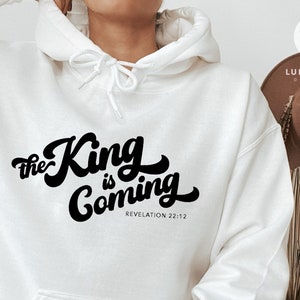 以下が含まれることがあります： 「The King is Coming」と「Revelation 22:12」という黒い文字が書かれた白いパーカー。
