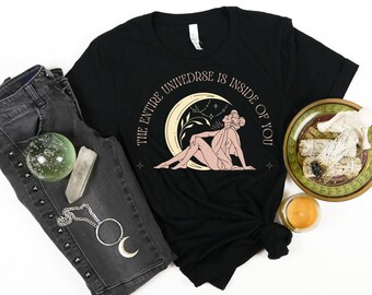 May include: Black t-shirt with a graphic of a woman sitting on a crescent moon with stars and the text "The entire universe is inside of you".