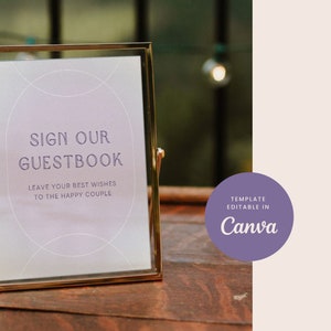 Puede incluir: Un cartel con marco dorado, fondo morado y texto blanco que dice "Sign Our Guestbook. Leave your best wishes to the happy couple." El cartel está sobre una mesa de madera. El texto "Template Editable in Canva" está en un círculo morado en la esquina superior derecha de la imagen.