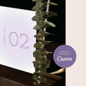 Puede incluir: Una tarjeta de número de mesa de color morado y blanco con el texto "Table No. 02" en una fuente moderna. La tarjeta está sobre una superficie de madera con vegetación en el fondo. El texto "Template Editable in Canva" está en un círculo morado en la esquina superior derecha.