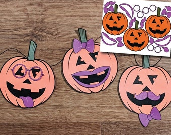 Op de afbeelding: Drie oranje papieren pompoen-uitknipsels met verschillende gezichtsuitdrukkingen. De pompoenen zijn aan elkaar geregen met zwart touw. De eerste pompoen heeft een paarse bril en een paarse tong die uitsteekt. De tweede pompoen heeft een paarse strik en een paarse mond. De derde pompoen heeft een paarse snor en een paarse vlinderdas.