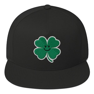 May include: Black and green embroidered four-leaf clover with a smiley face on a black fitted baseball cap.