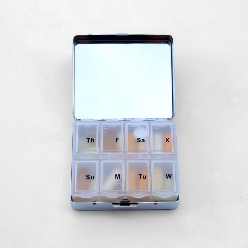 Puede incluir: Una caja de pastillas de plata con un espejo en la parte superior. La caja de pastillas tiene siete compartimentos etiquetados con los d&iacute;as de la semana: Su, M, Tu, W, Th, F, Sa.