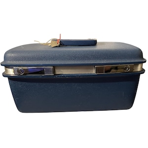 May include: A vintage navy blue suitcase with a textured surface, silver trim, and two metal latches. A small handle and a set of keys are on top. The suitcase is rectangular with rounded edges.