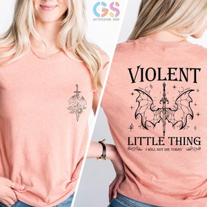 May include: A peach-colored t-shirt with a black graphic of a sword and wings on the front and the text "VIOLENT LITTLE THING I WILL NOT DIE TODAY" on the back.