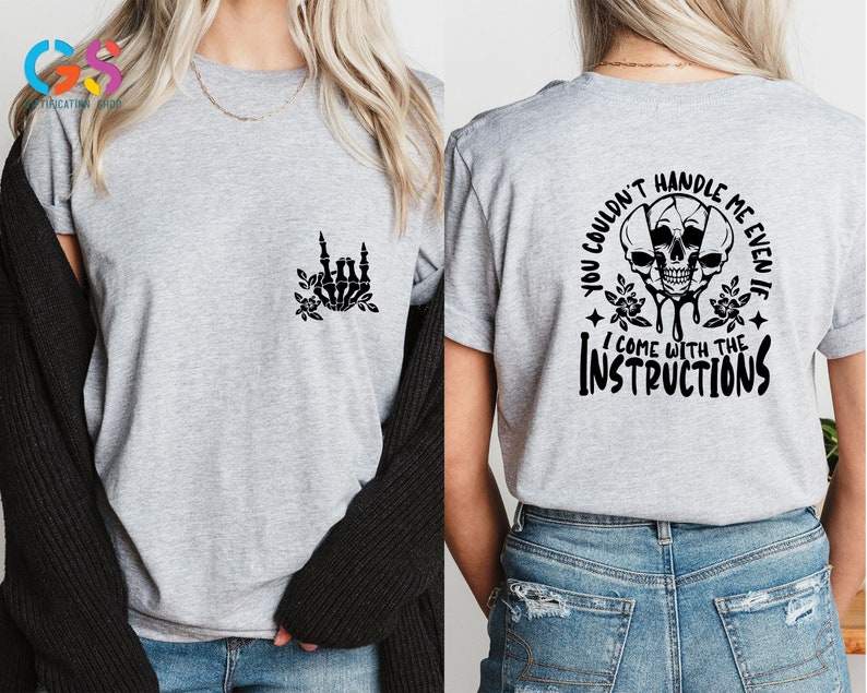 Op de afbeelding: Grijs T-shirt met een zwarte skelet hand die een rock and roll-teken maakt aan de linkerkant en de tekst "You couldn't handle me even if I come with the instructions" met een zwarte schedel afbeelding aan de rechterkant.