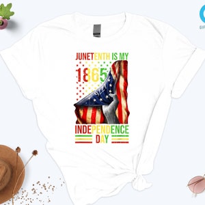 Puede incluir: Camiseta blanca con un dise&ntilde;o gr&aacute;fico que celebra el Juneteenth. El dise&ntilde;o incluye el texto "Juneteenth is my Independence Day 1865" con una bandera americana y estrellas. La camiseta es una prenda informal.