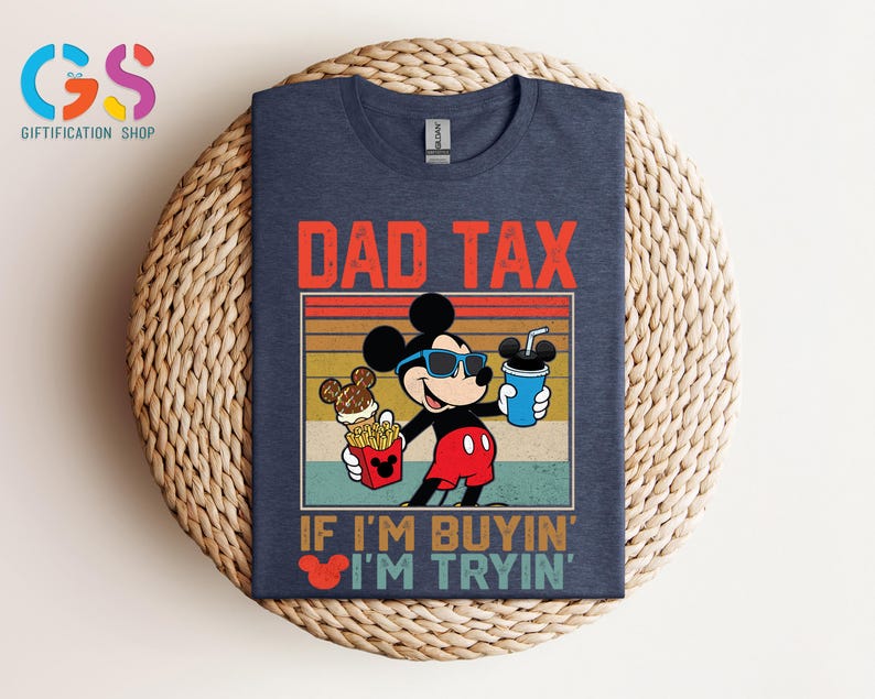 May include: Navy blue t-shirt featuring Mickey Mouse wearing sunglasses and holding food and a drink. The text "DAD TAX" is above the image, and "IF I'M BUYIN' I'M TRYIN'" is below. The shirt is displayed on a woven surface.