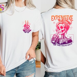 May include: White t-shirt with a pink and purple skull graphic and the text "Expensive and Talks Back".