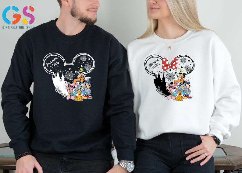 Pode incluir: Camisolas pretas e brancas com um design de cabe&ccedil;a do Mickey Mouse com personagens da Disney. A camisola preta tem impresso "Andrew 2026", enquanto a camisola branca tem "Sophia 2026". Ambas t&ecirc;m a palavra "Disney" impressa.