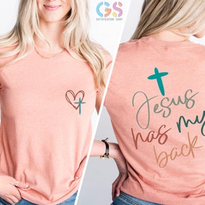 May include: A peach-colored t-shirt with a heart and cross design on the front and the text "Jesus has my back" with a cross on the back.