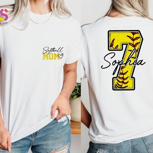 May include: White t-shirt with the text "Softball Mom" and a heart on the front. The back of the shirt has a yellow softball with red stitching and the number 7 with the name "Sophia" underneath.