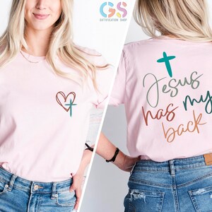 May include: Pink t-shirt with a heart and cross on the front and the text "Jesus has my back" on the back. The text is in a variety of colors, including green, brown, and orange.