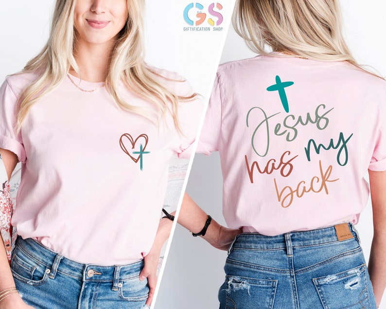 May include: Pink t-shirt with a heart and cross on the front and the text "Jesus has my back" on the back. The text is in a variety of colors, including green, brown, and orange.