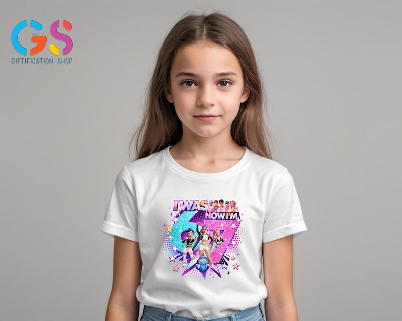 以下が含まれることがあります： 「I WAS 6 NOW I'M 7」の文字が入ったカラフルなグラフィックデザインの白いTシャツ。2人の女の子と星のイラストが幾何学模様の背景に配置されています。Tシャツを着ているのは若い女の子です。