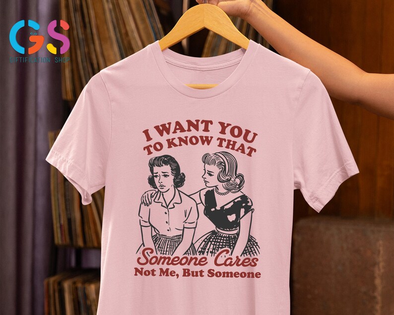 Op de afbeelding: Roze T-shirt met een afbeelding van twee vrouwen. De tekst op het shirt luidt "I want you to know that Someone Cares Not Me, But Someone".