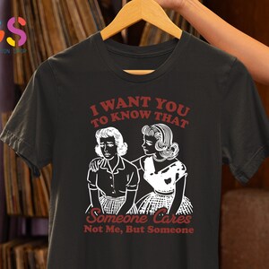 Op de afbeelding: Zwart T-shirt met een witte afbeelding van twee vrouwen. De tekst op het shirt luidt "Ik wil dat je weet dat iemand geeft, niet ik, maar iemand."