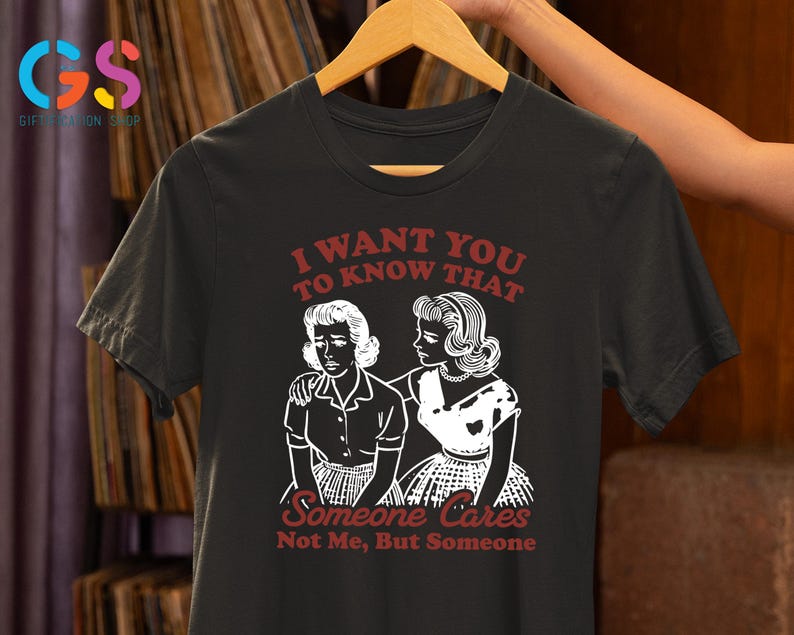 Op de afbeelding: Zwart T-shirt met een witte afbeelding van twee vrouwen. De tekst op het shirt luidt "Ik wil dat je weet dat iemand geeft, niet ik, maar iemand."