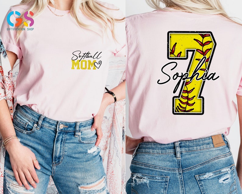 May include: Pink softball mom t-shirt with a gold glitter design that says "Softball Mom" with a heart. The back of the shirt has a yellow softball with red stitching and the number 7 with the name "Sophia" written in black cursive.