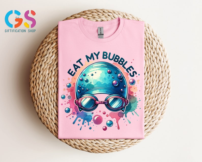 May include: Pink t-shirt with a colorful graphic of a swimmer's cap and goggles with the text "Eat My Bubbles".